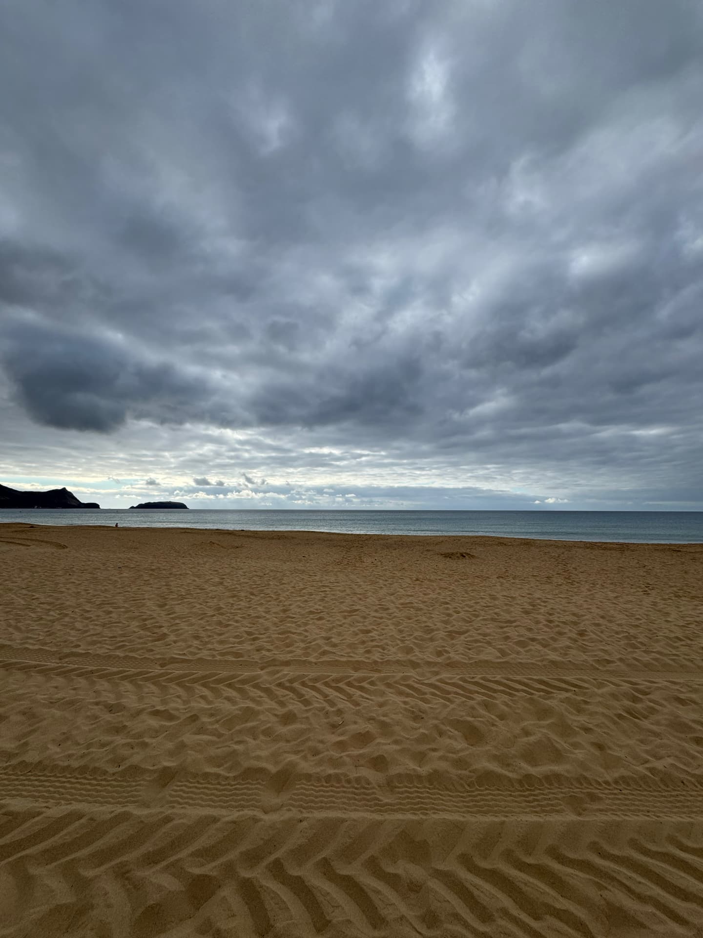 Tire tracks in an empty sandy Beach with the ocean just ahead.